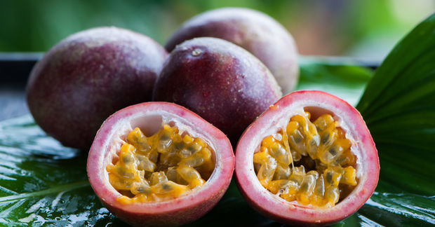 photo Fresh passion fruits, one cut in half revealing golden seedy pulp, displayed on a green tropical leaf outdoors.
