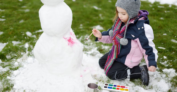 photo Child painting snowman with colorful paints outdoors.