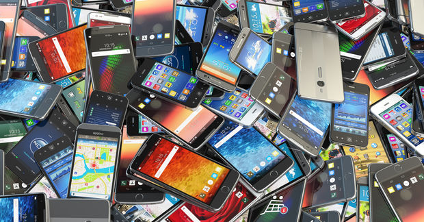 photo A large pile of various smartphones with colorful screens, different brands and sizes, stacked haphazardly together.