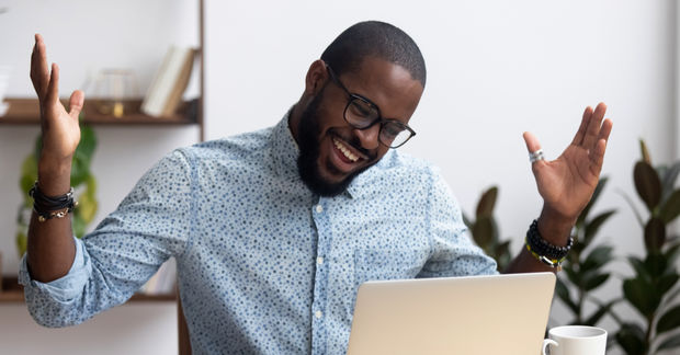 photo man looks happy raising hands infront of a laptop