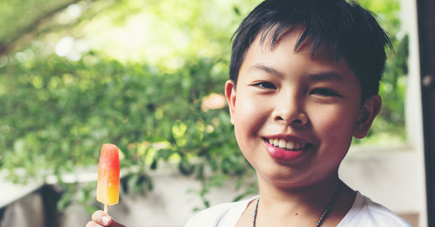 photo Happy boy eating colorful popsicle outdoors.