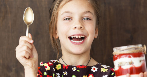 photo Happy girl with spoon and layered dessert jar.