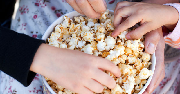 photo Hands reaching for popcorn in bowl.