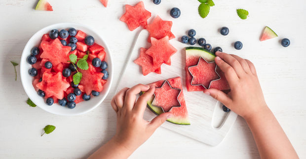 photo Hands cutting star-shaped watermelon with blueberry bowl.