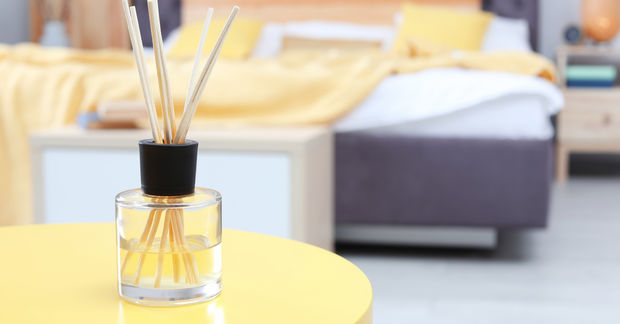 photo A reed diffuser with wooden sticks in a glass bottle sits on a yellow table in a cozy bedroom.