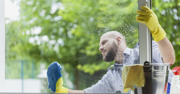 photo A man wearing yellow rubber gloves washes a large window with a blue cloth and soapy water.