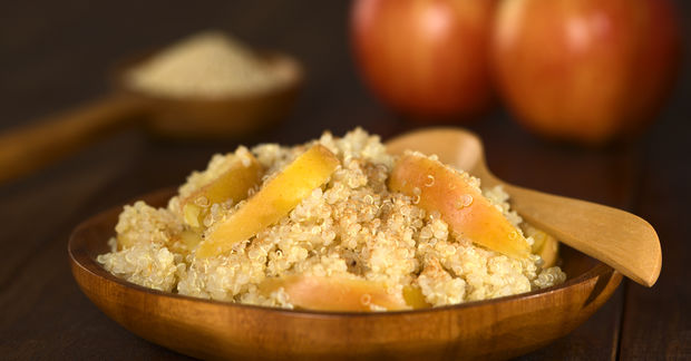 Quinoa Bowl of quinoa topped with dried apricot slices with a wooden spoon, with blurred onions in the background.