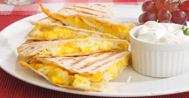 This Cheese quesadillas cut into triangles on a white plate served with sour cream dip and red grapes.