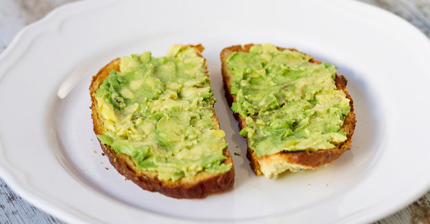 Avocado Two slices of toasted bread topped with mashed avocado on a white plate.