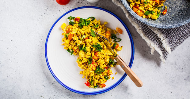 This Scrambled eggs with corn, red peppers, and green herbs in a white bowl with blue rim on a concrete surface.
