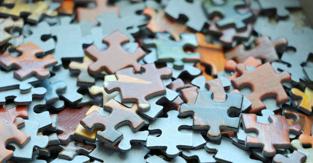 Scattered colorful puzzle pieces in blue, pink, orange, and yellow scattered across a light blue surface in shallow focus.