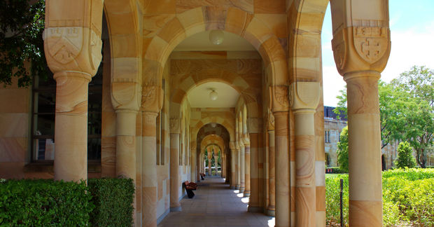 University The University of Queenland, Long stone colonnade with arched ceiling and decorative columns, with ivy on the sides and bright daylight at the end of the corridor.
