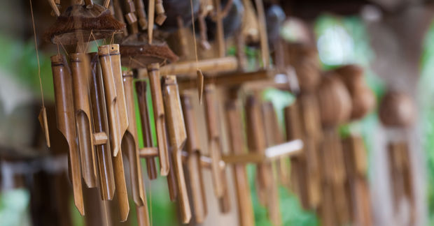 Wooden Multiple handcrafted bamboo wind chimes hanging in a row with a soft-focus green background.
