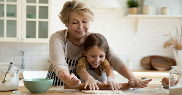 Grandmother Grandmother and granddaughter baking together in a bright kitchen, kneading dough on a counter with bowls and ingredients around them.